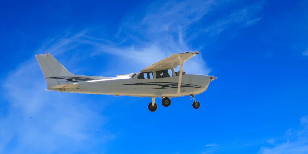 A small single-engine airplane with its landing gear down flies against a clear blue sky.