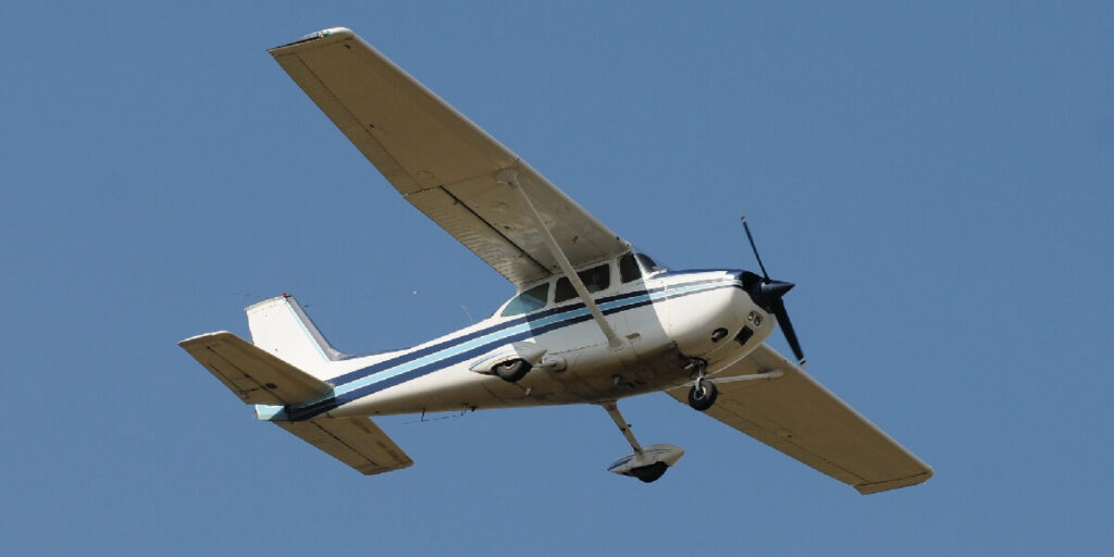 A small single-engine airplane banks in flight against a clear blue sky.