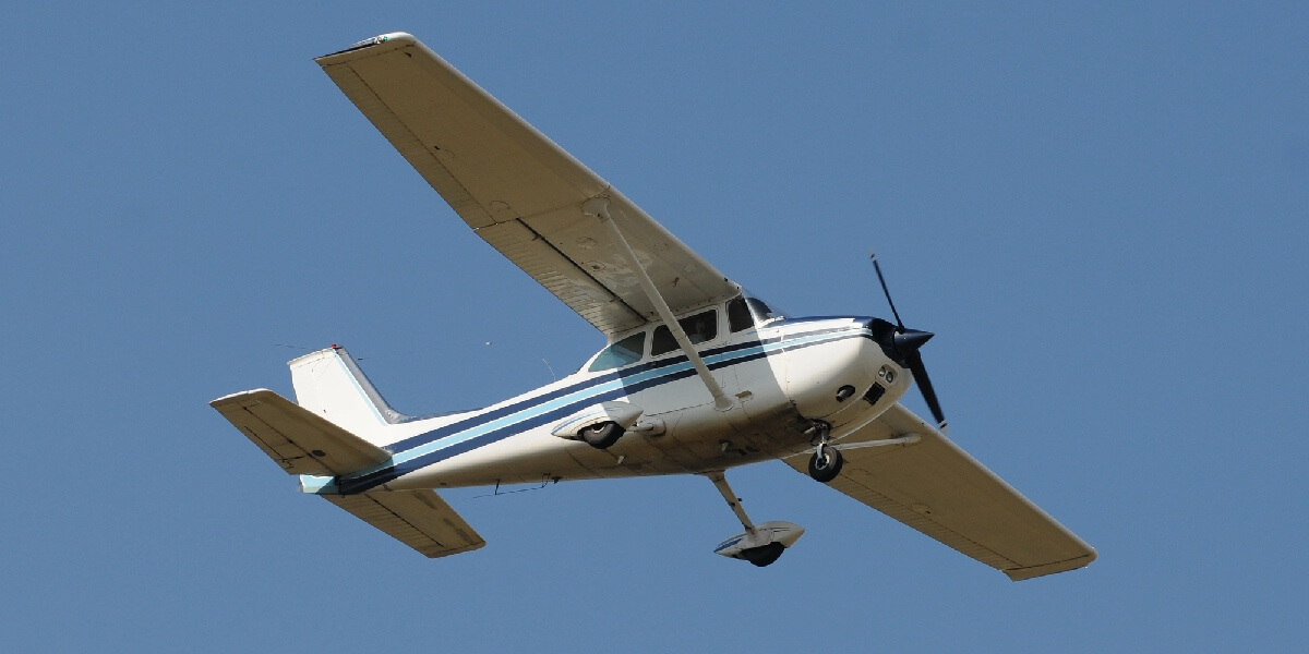 A small single-engine airplane banks in flight against a clear blue sky.