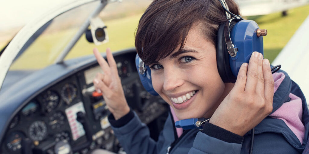 A smiling female pilot flashes a peace sign while sitting in a small plane's cockpit.